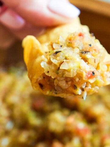 A wood bowl with a lady scooping out homemade salsa with a tortilla chip.