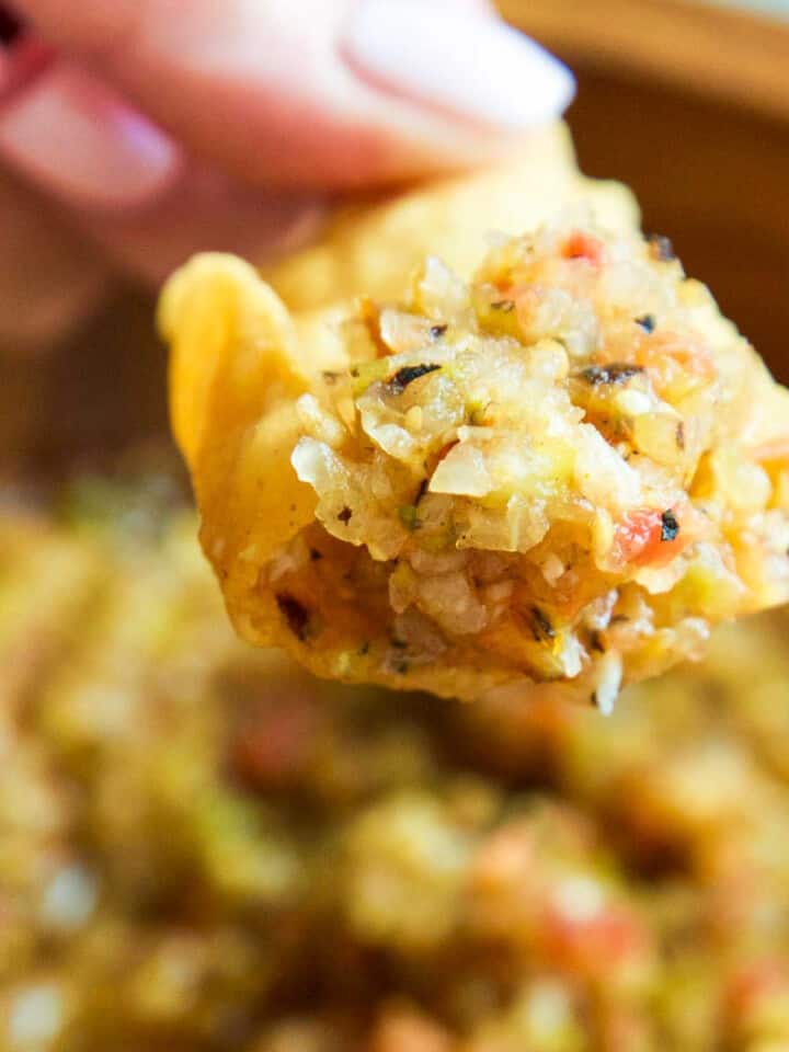 A wood bowl with a lady scooping out homemade salsa with a tortilla chip.