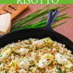 A large vintage cast iron skillet with cooked arborio rice risotto and artichokes topped with pine nuts, grated parmesan cheese and chives