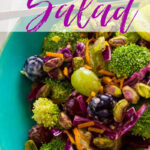 A turquoise blue bowl with with a bright colorful broccoli salad filled with tri-color grapes, purple cabbage, broccoli, green apple, and a creamy orange dressing.