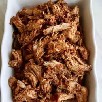 A white casserole dish with oven roasted pork loin shredded and ready to eat in tacos or a recipe for dinner.
