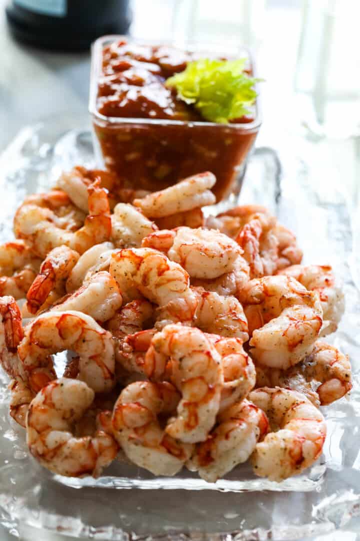 2 lbs of cooked shrimp on a glass platter with cocktail to serve at a party.