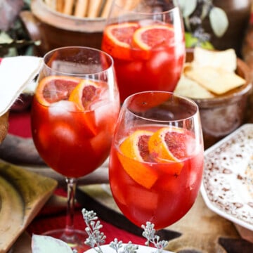 Three glasses of aperol spritz Fall cocktails with appetizers nearby on a table at an outdoor party.