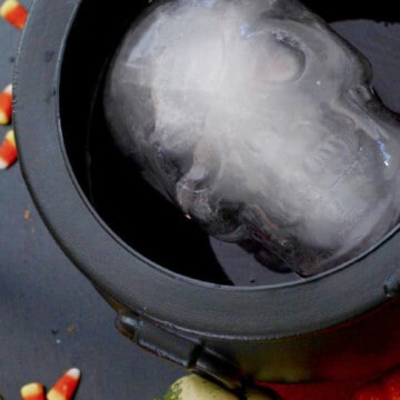 A black witches cauldron filled with Halloween Punch and a frozen spooky ice skull on a black table at a Halloween party. t