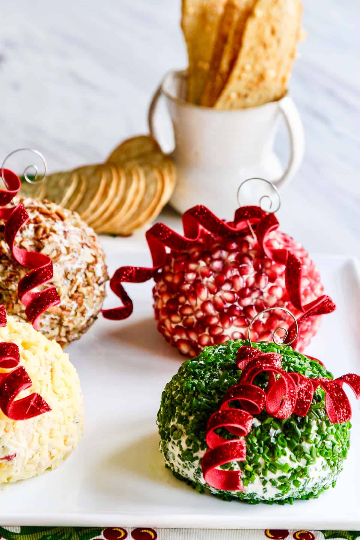 Vier felgekleurde ronde kaasballetjes belegd met toppings en versierd als kerstboomornamenten om te serveren op een feestdag met crackers. 