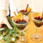 A lady holding a tray of mulled wine garnished with cinnamon sticks and orange peel.