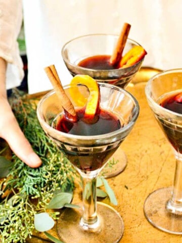 A lady holding a tray of mulled wine garnished with cinnamon sticks and orange peel.