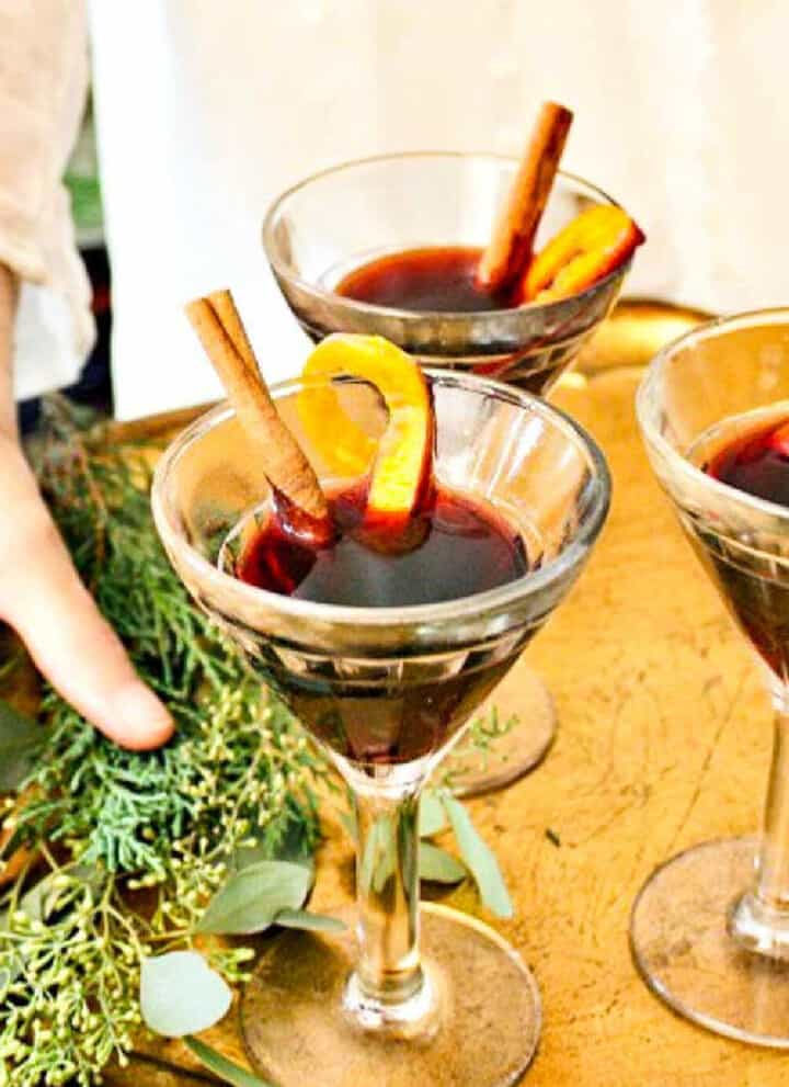 A lady holding a tray of mulled wine garnished with cinnamon sticks and orange peel.