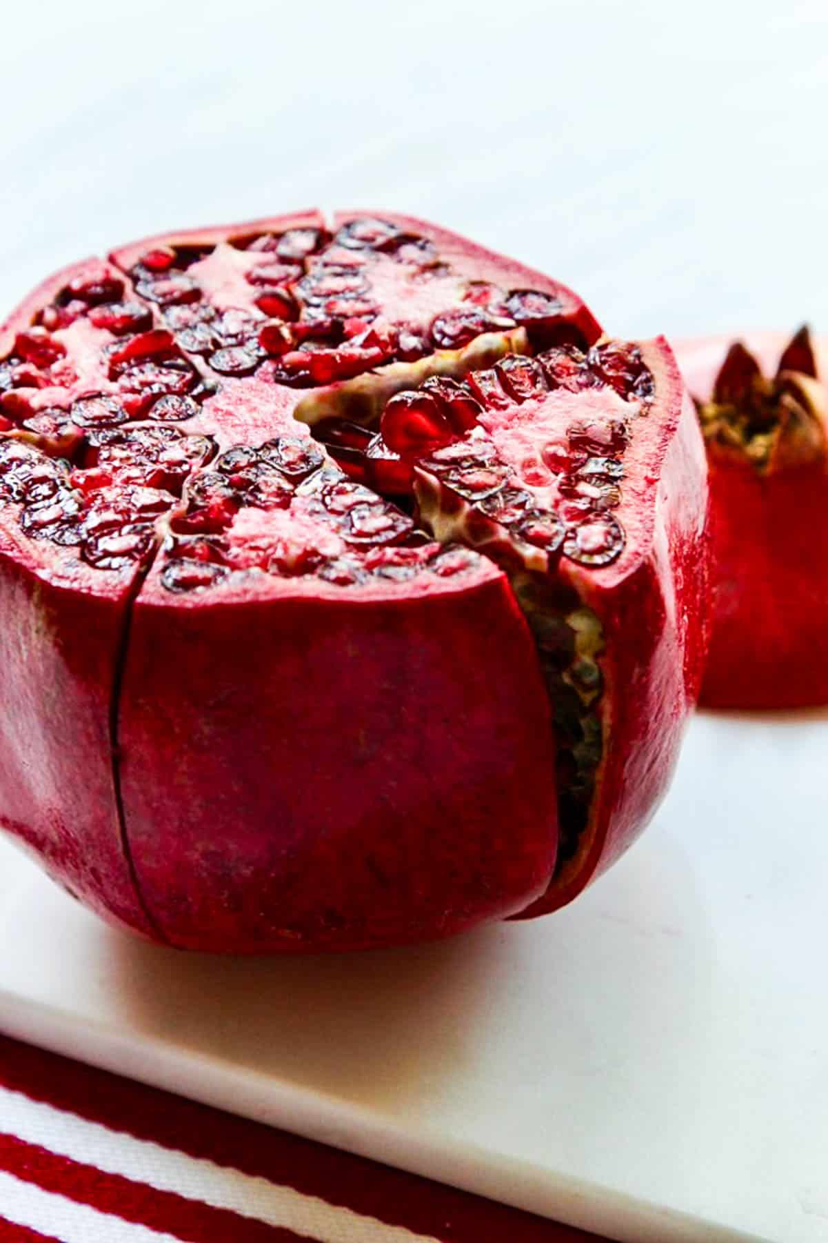 A large red pomegranate with the top cut off and cut down the side.