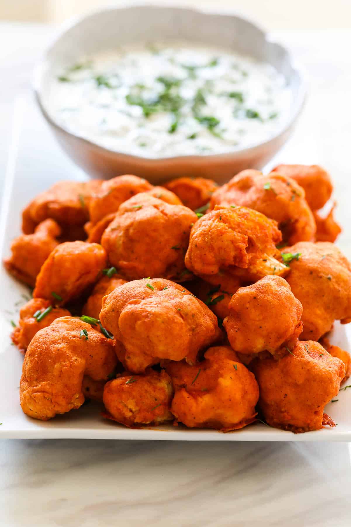 Baked Buffalo Cauliflower on a plate with ranch dip sprinkled with fresh herbs.