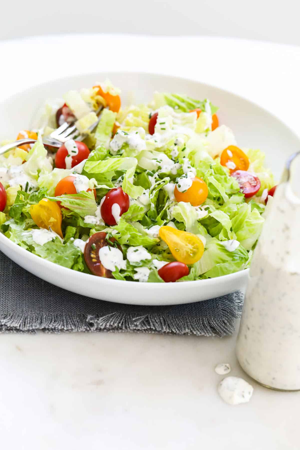 A white round plate filled with colorful green salad topped with ranch dressing.