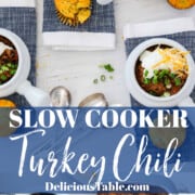 White bowls of turkey chili topped with cheese, sour cream, and green onions.