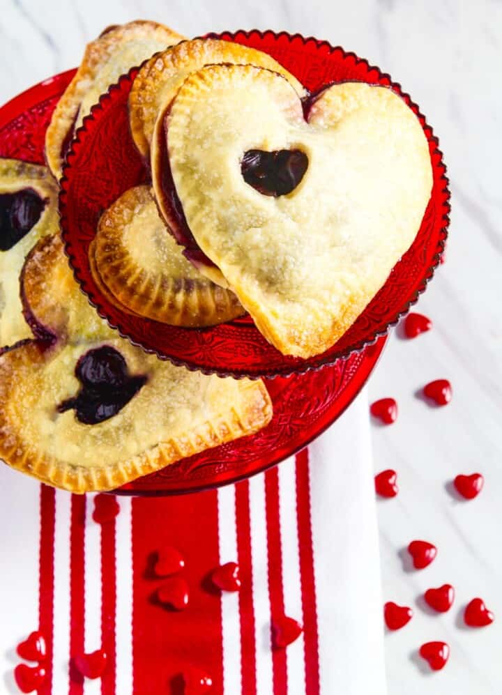 A stack of heart shaped hand pies on red plates with red and white decorations.