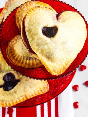 A red cookie plate filled with heart shaped chocolate hand pies.