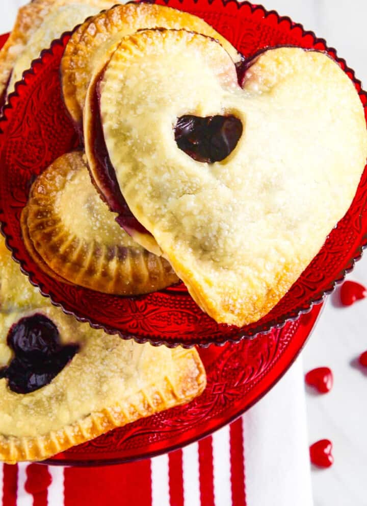 A red cookie plate filled with heart shaped chocolate hand pies.