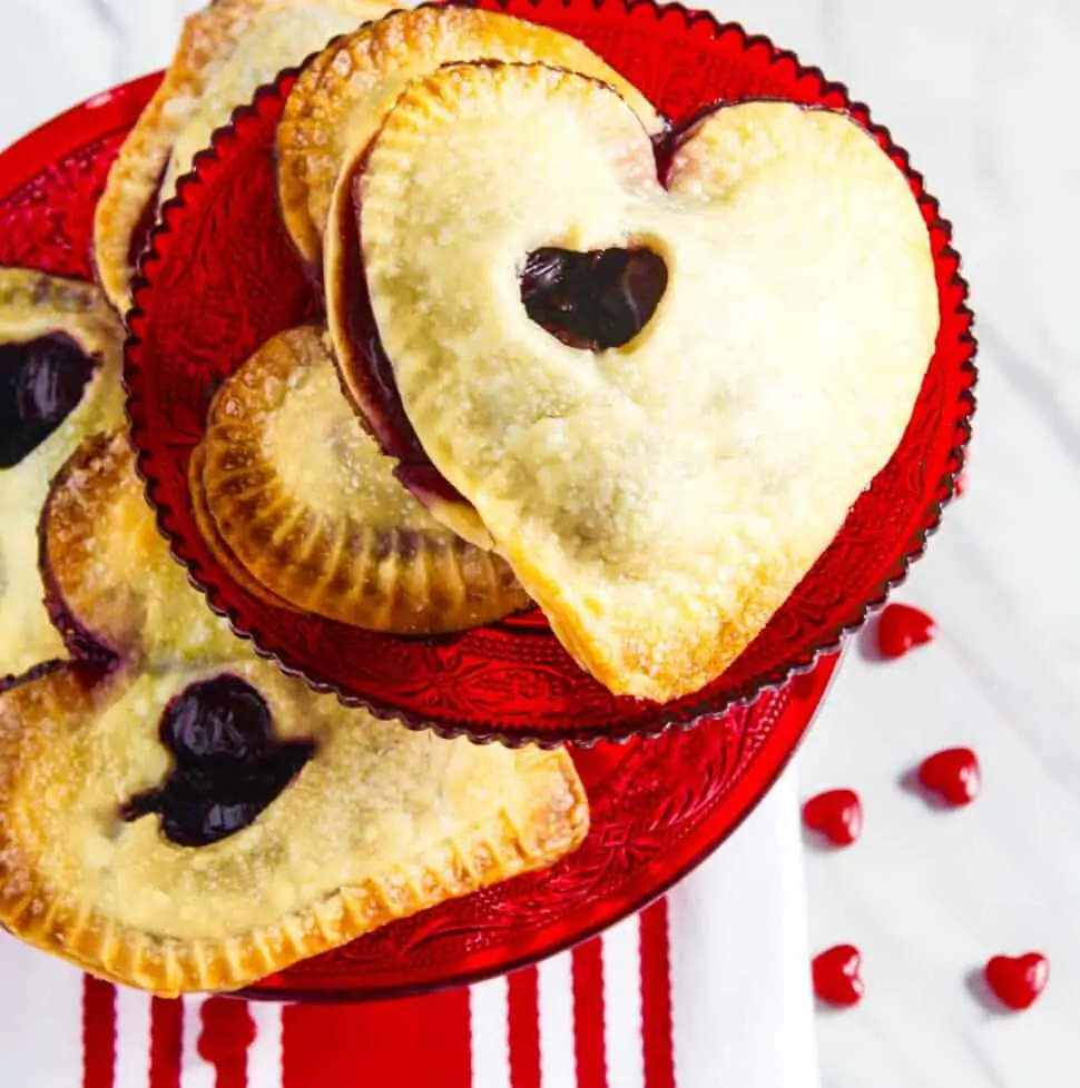 A red cookie plate filled with heart shaped chocolate hand pies.