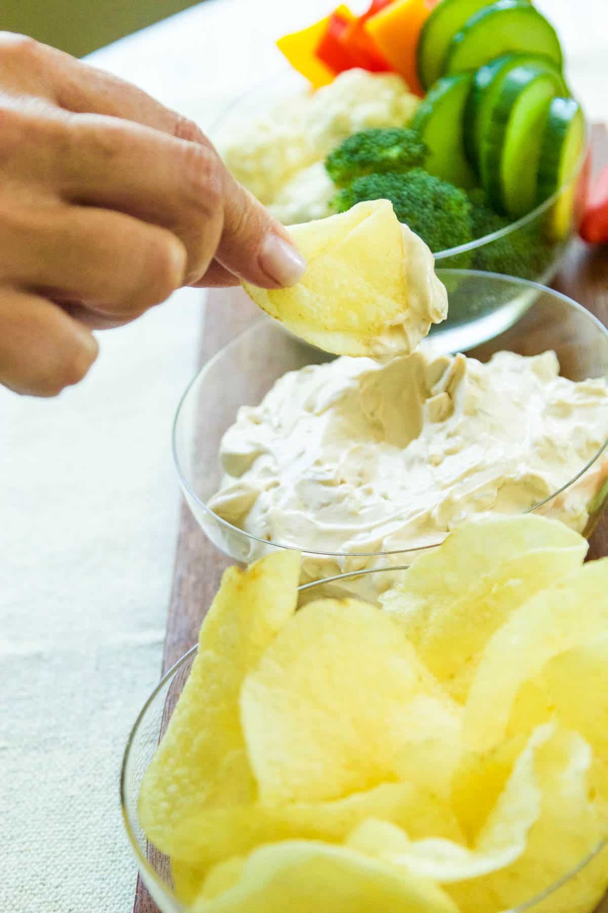 A lady dipping a potato chip into onion dip.