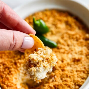Scooping out a bite of hot dip from a white dish of freshly baked jalapeno popper dip.