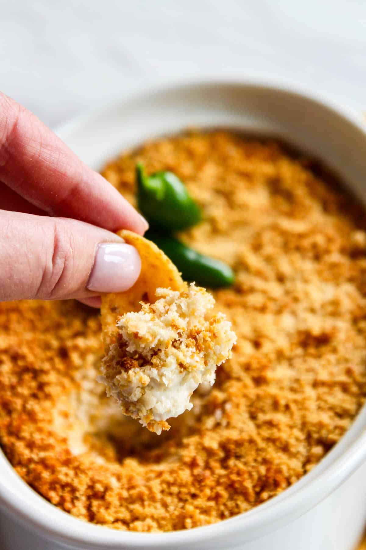 Scooping out a bite of hot dip from a white dish of freshly baked jalapeno popper dip.