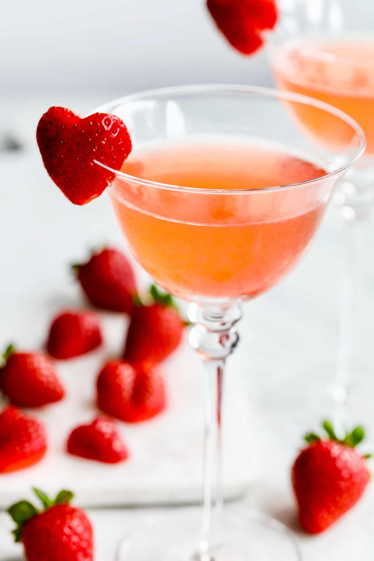 Heart shaped garnish made from strawberry on edge of pink cocktail.