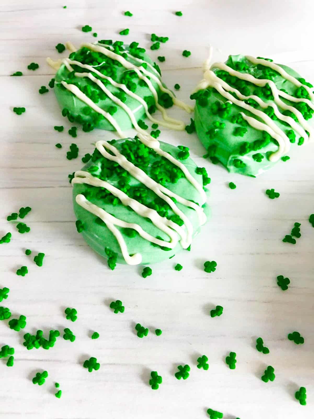 Three green oreos dipped in green chocolate topped with shamrocks sprinkles. 