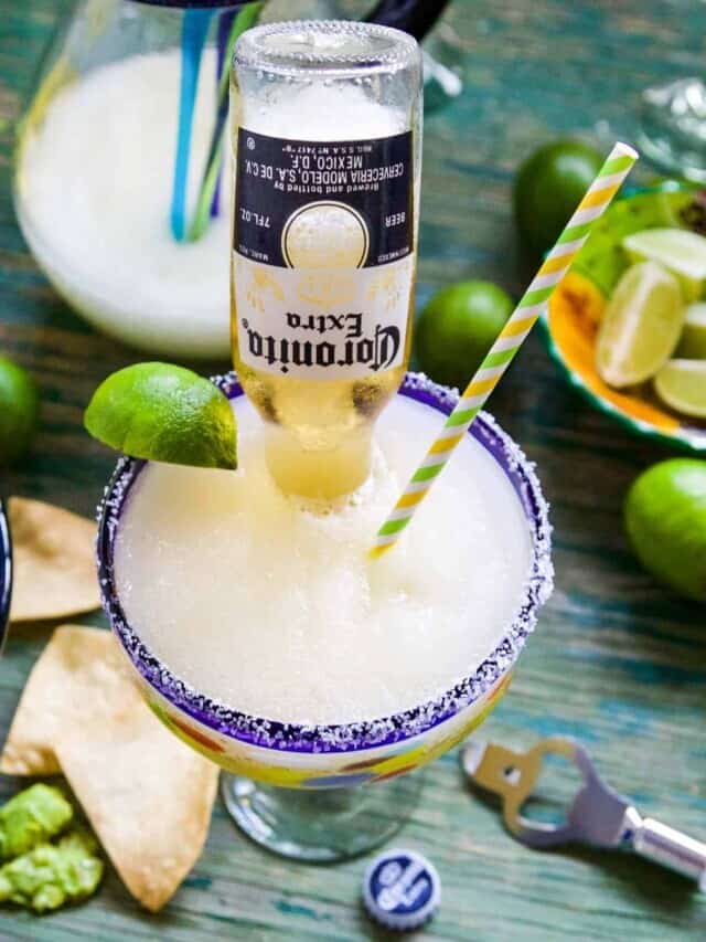 A blue rim margarita glass with a CoronaRita garnished with a lime wedge and straw.
