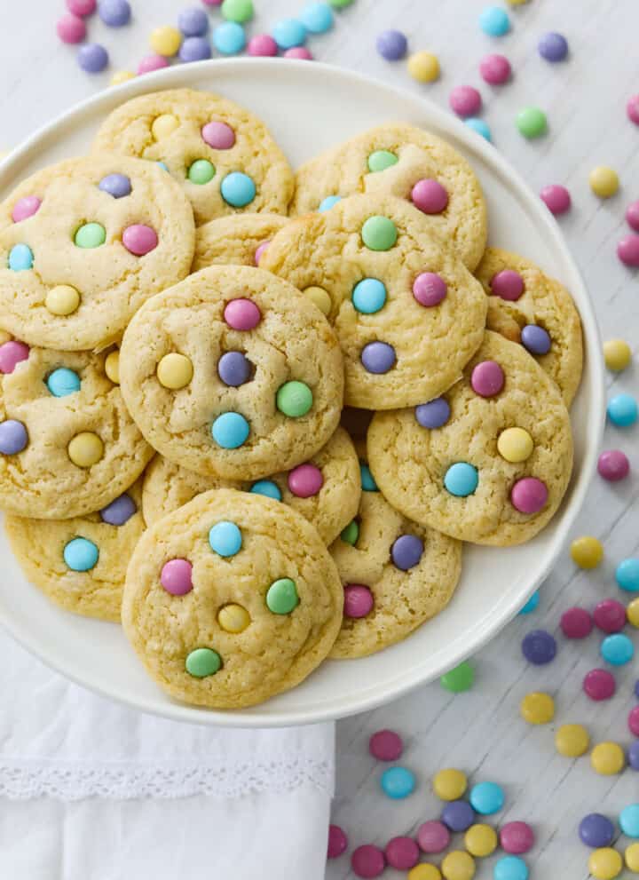 A white plate filled with freshly baked cake mix cookies with pastel m&m candies.