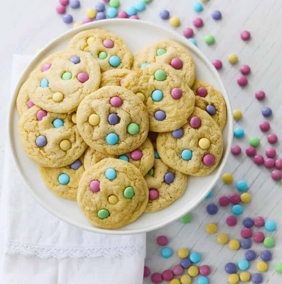 A white plate filled with freshly baked cake mix cookies with pastel m&m candies.