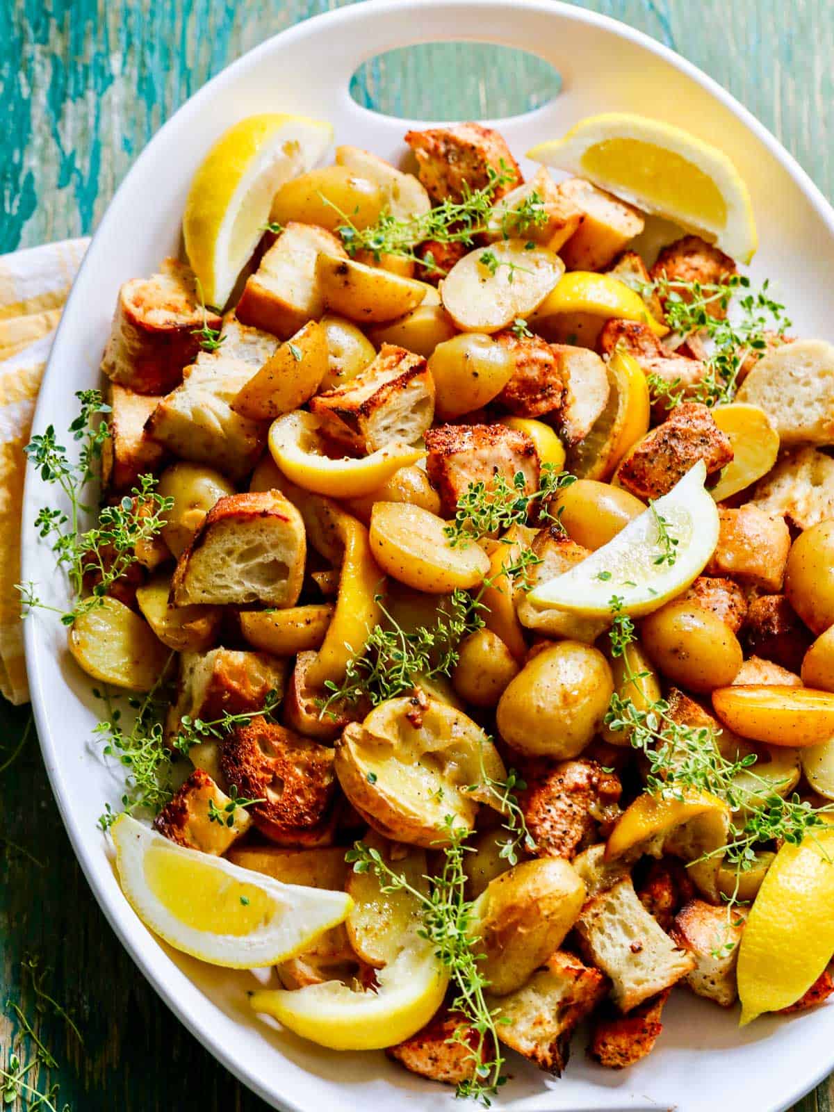 A large white oval platter filled with cooked sheet pan dinner including chicken, potatoes, lemons, and croutons.