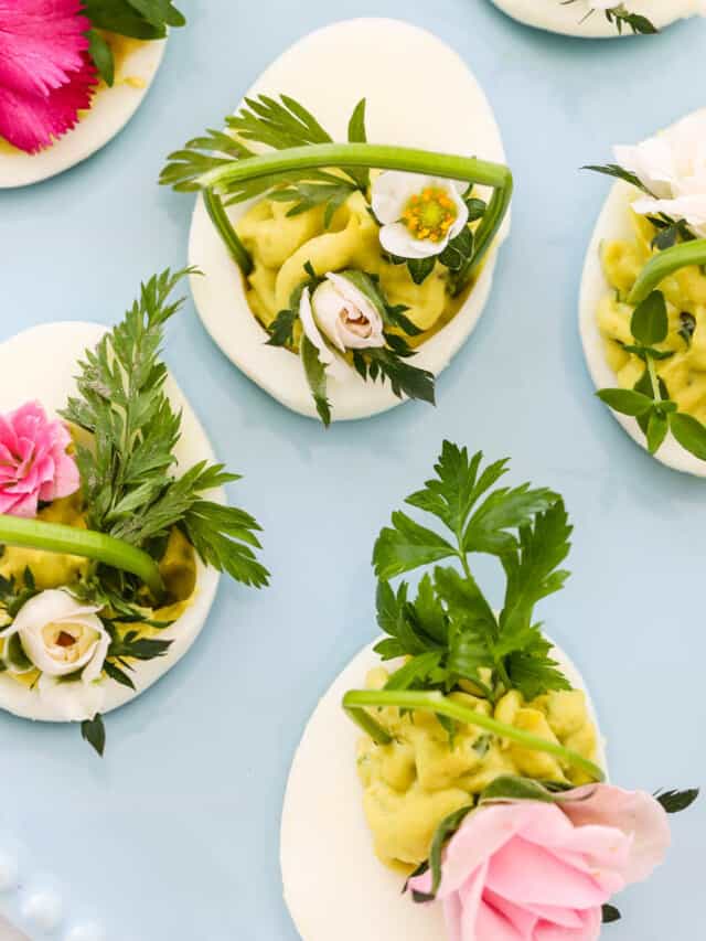 Pretty Easter deviled eggs with green filling and decorated with fresh herbs and edible flowers.