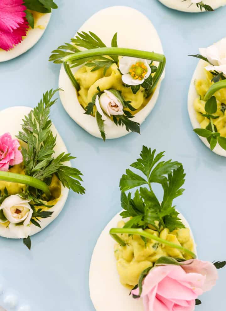 Pretty Easter deviled eggs with green filling and decorated with fresh herbs and edible flowers.