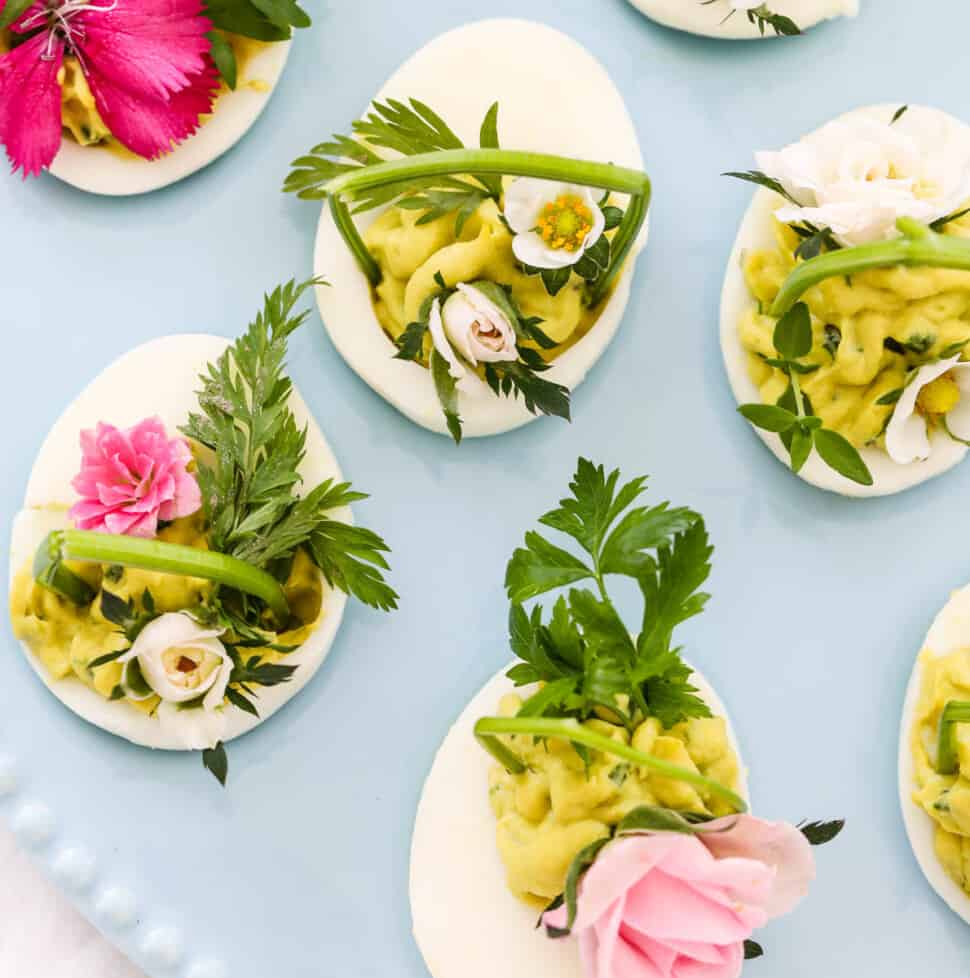 Pretty Easter deviled eggs with green filling and decorated with fresh herbs and edible flowers.