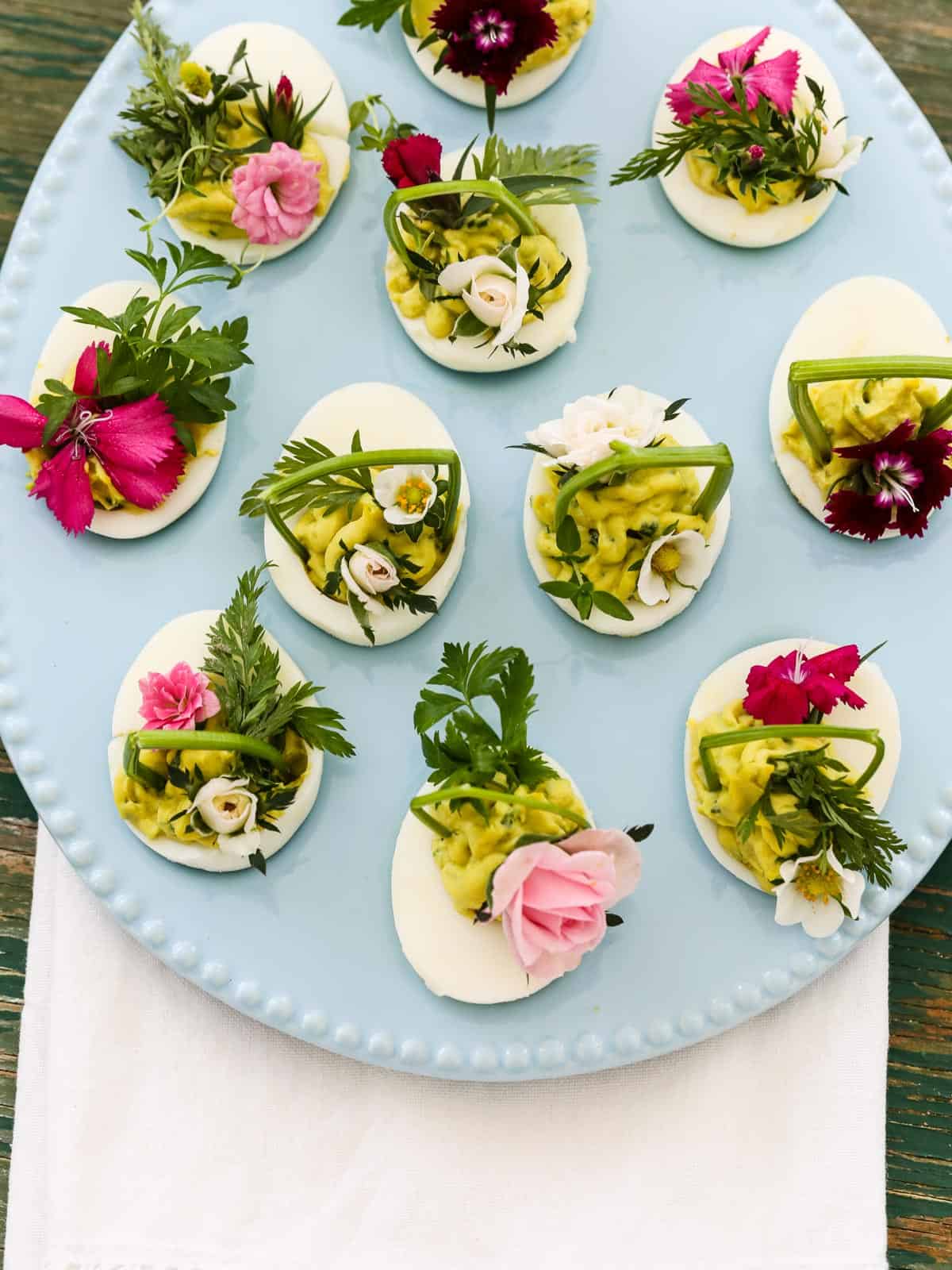 Looking down into a pastel blue egg shaped plate loaded with deviled eggs for Easter decorated with edible flowers and herbs.