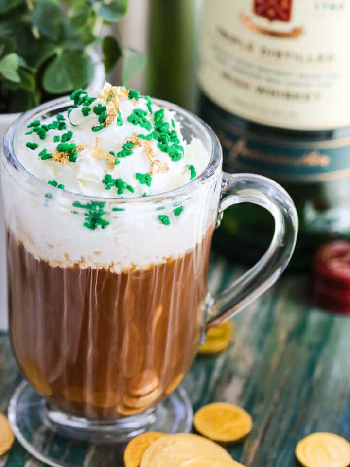 A glass mug with Irish Coffee on a vintage green table topped with green sprinkles and edible gold.