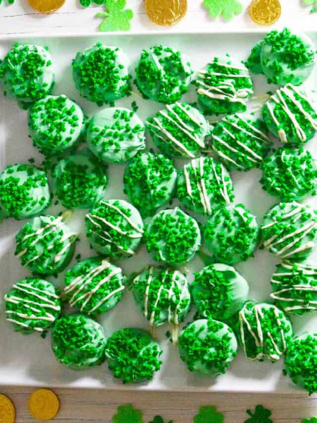A square white plate with green oreos decorated with shamrock sprinkles.