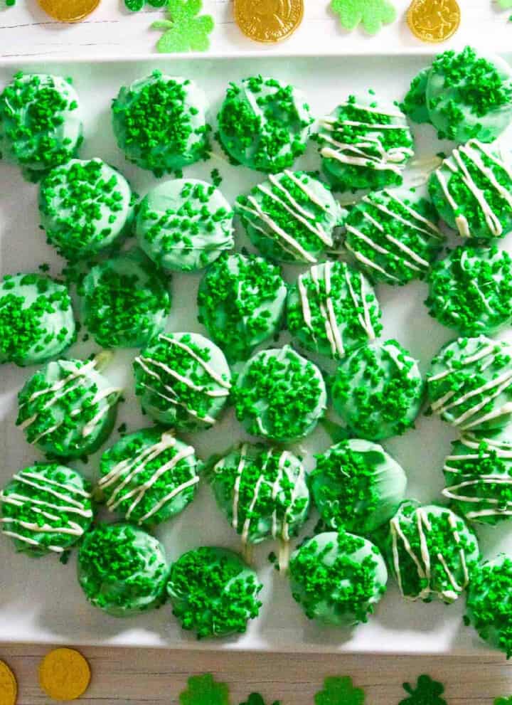 A square white plate with green oreos decorated with shamrock sprinkles.