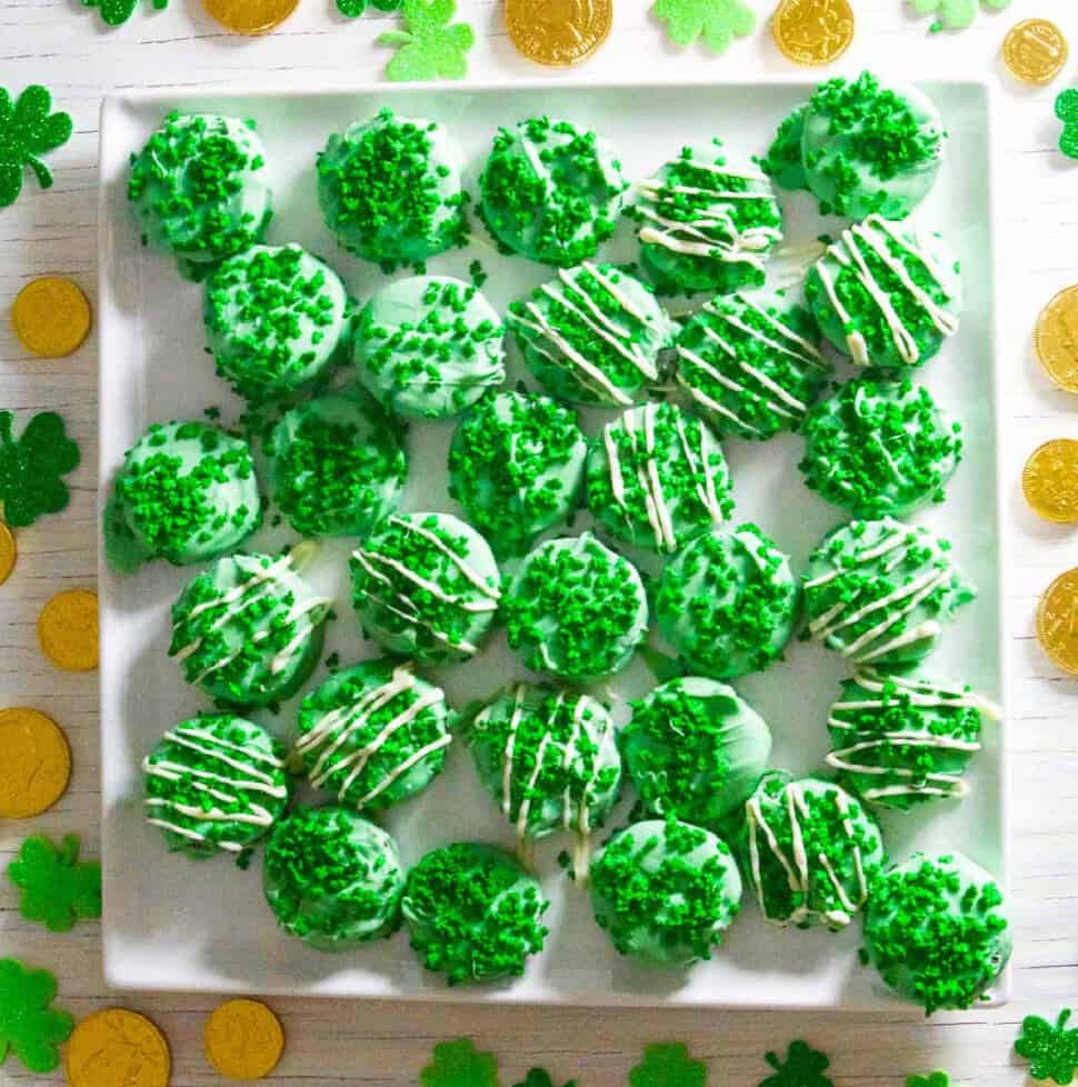 A square white plate with green oreos decorated with shamrock sprinkles.