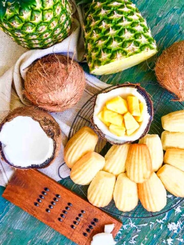 Overhead looking a madeleines cooled on a round baking rack with fresh pineapple and coconut fruit.