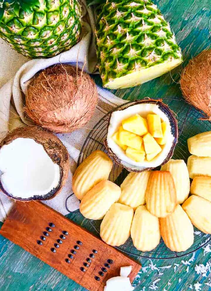 Overhead looking a madeleines cooled on a round baking rack with fresh pineapple and coconut fruit.