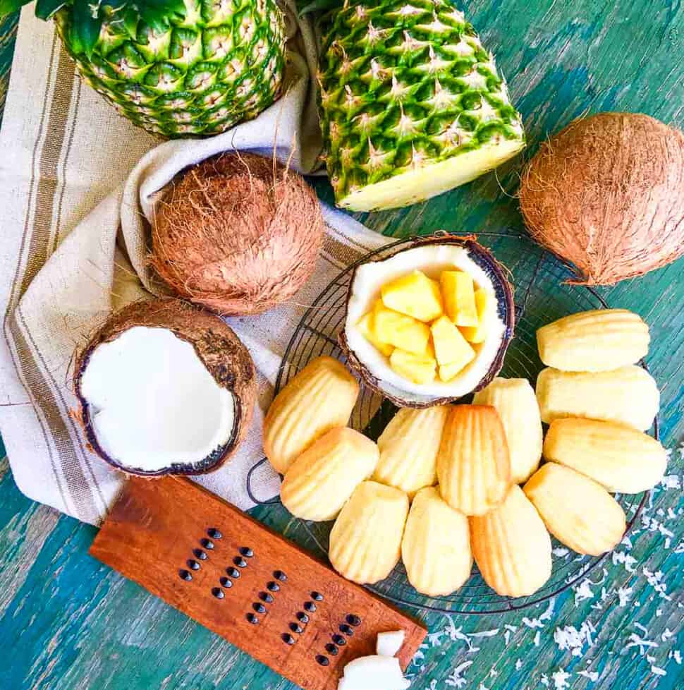 Overhead looking a madeleines cooled on a round baking rack with fresh pineapple and coconut fruit.