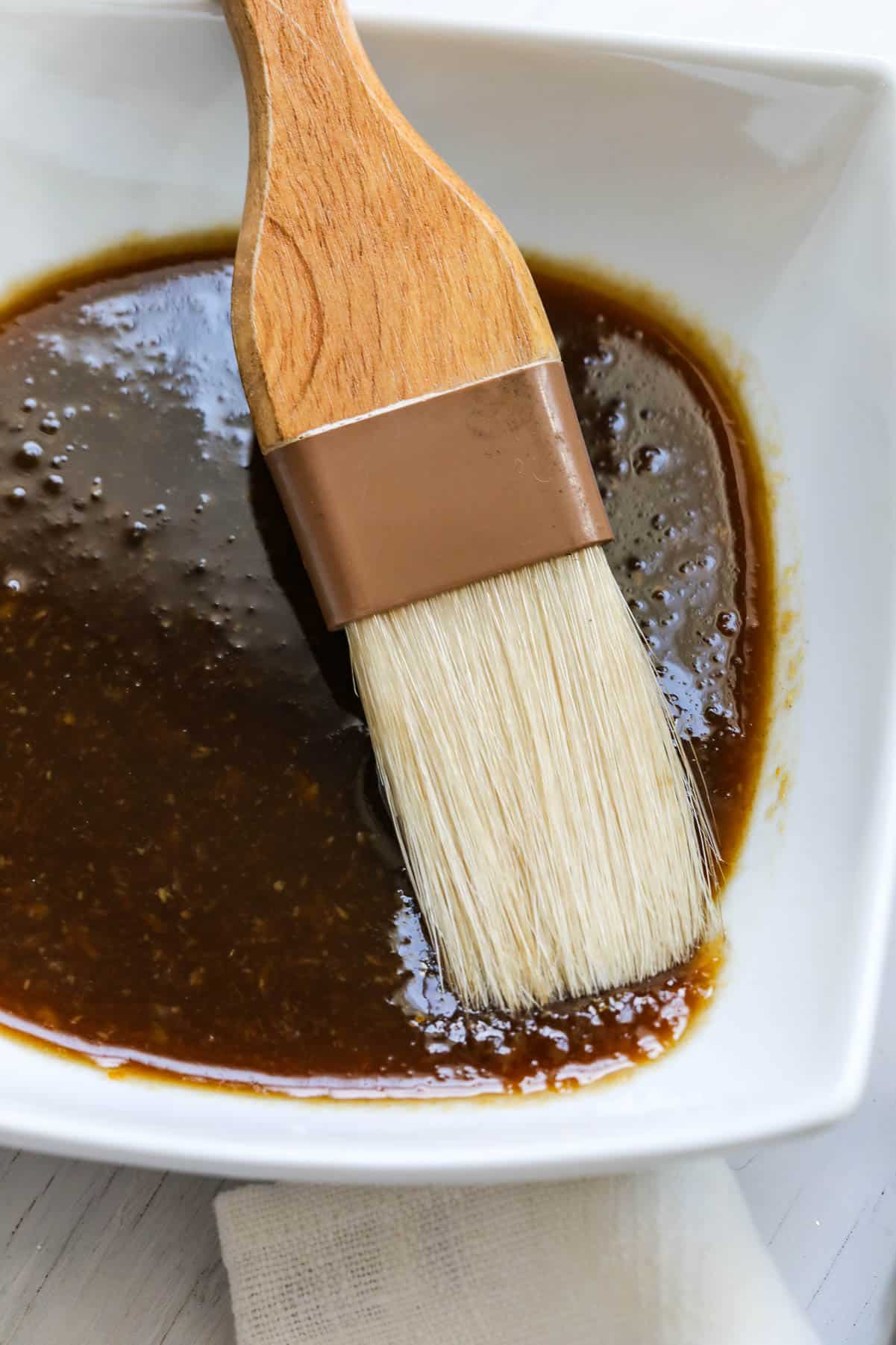 A white bowl with a large flat brush in ham glaze to make a ham recipe.