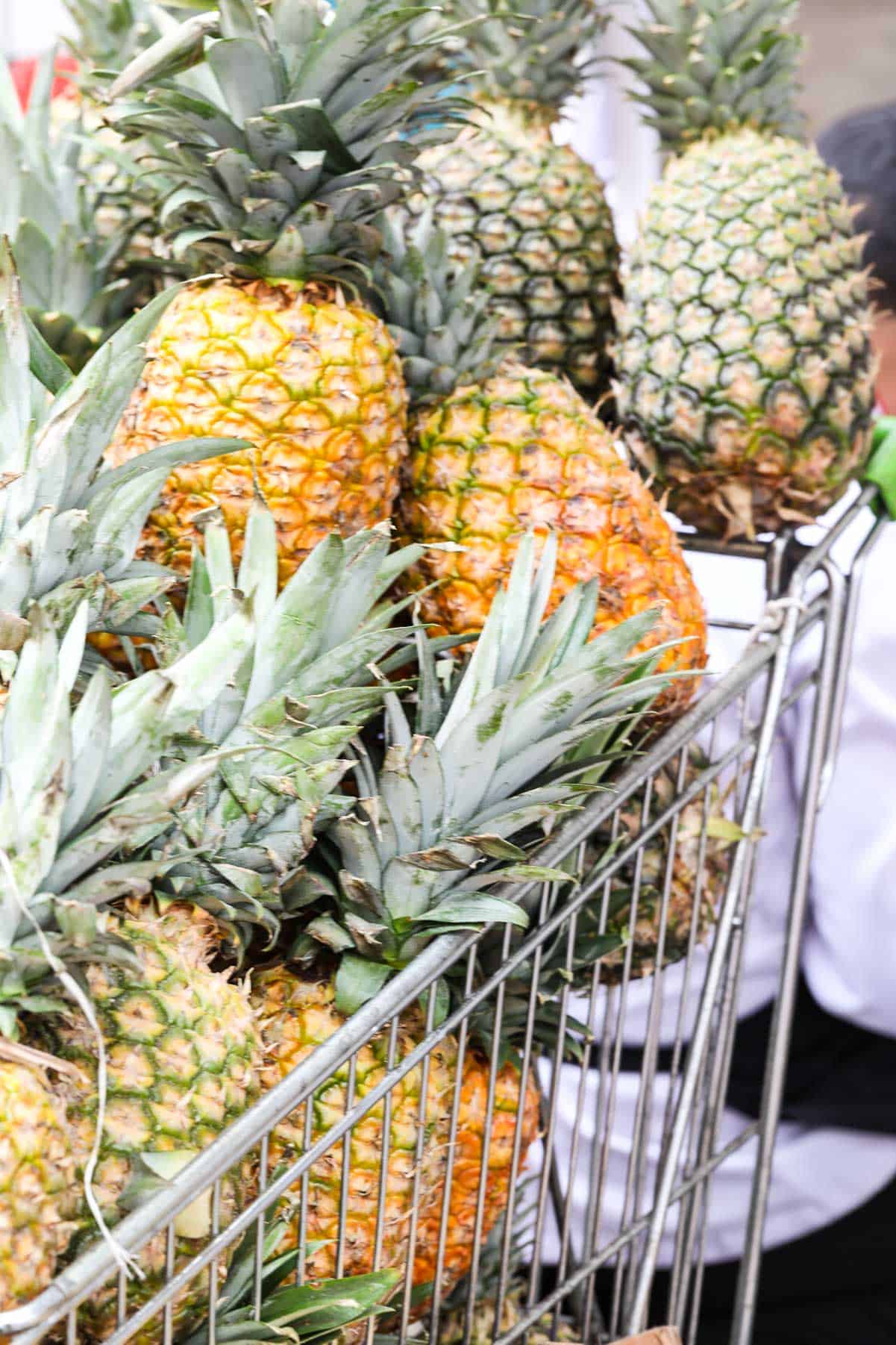 A steel grocery cart filled with fresh ripe whole pineapples in a market.