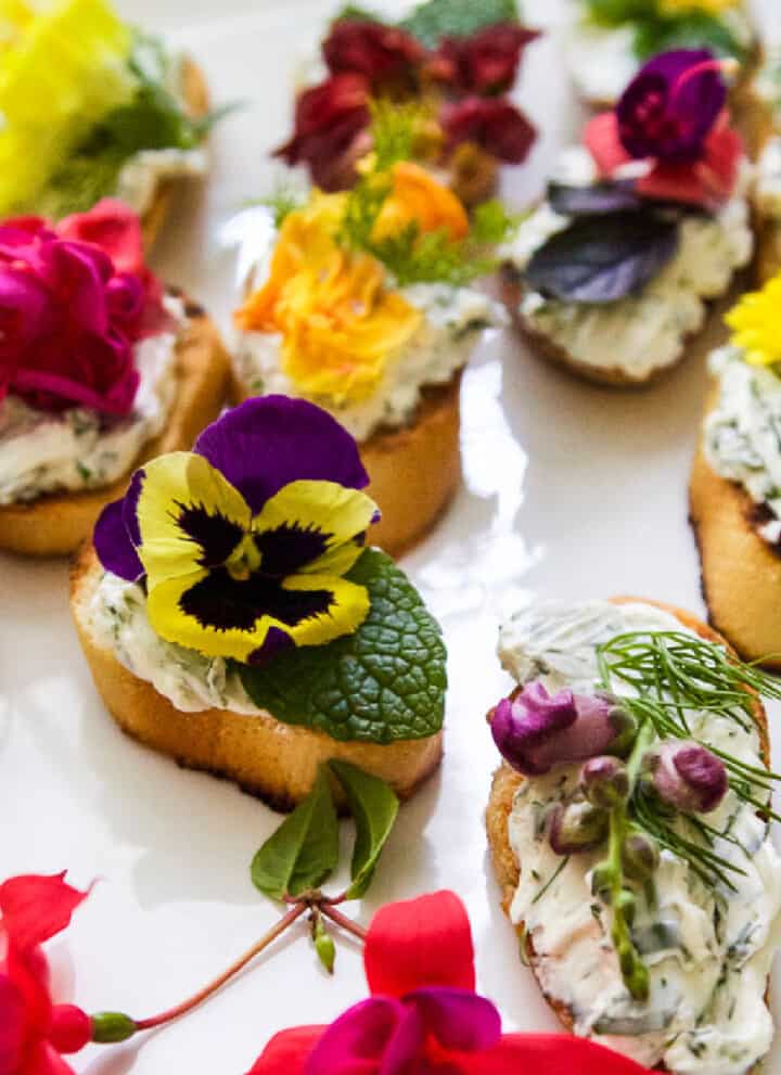 A white platter with crostini recipe topped with edible flowers and herbs.