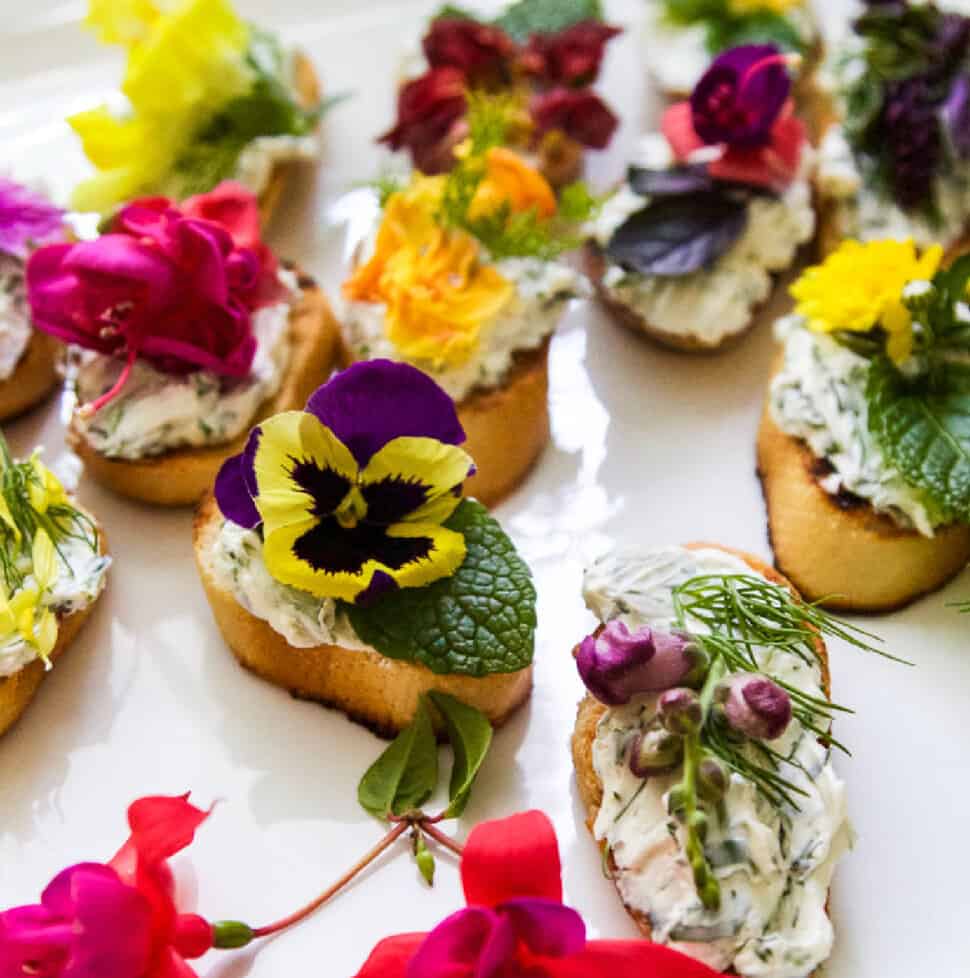 A white platter with crostini recipe topped with edible flowers and herbs.