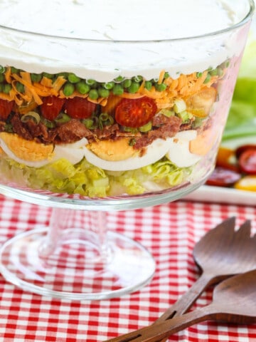 A glass trifle dish filled with 7 Layer Salad full of colorful ingredients.