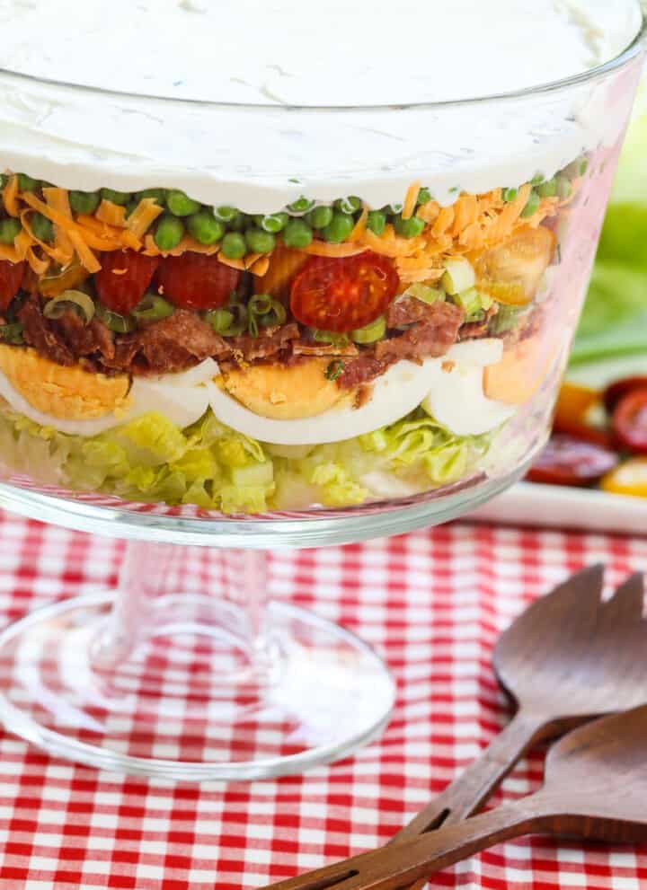 A glass trifle dish filled with 7 Layer Salad full of colorful ingredients.