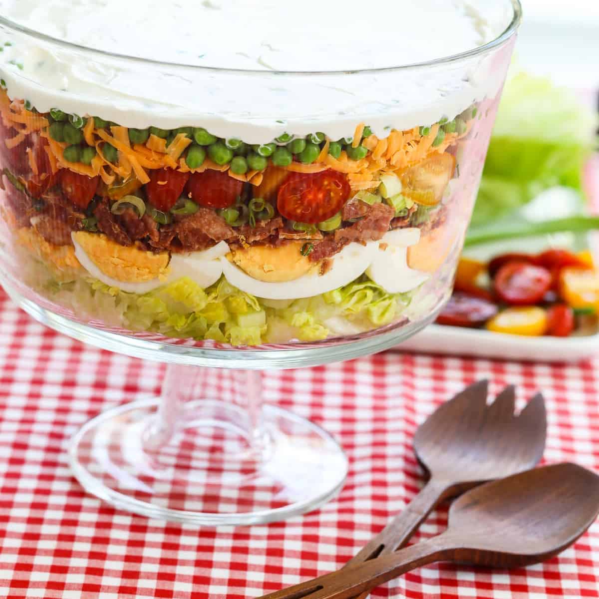 A glass trifle dish filled with 7 Layer Salad full of colorful ingredients.