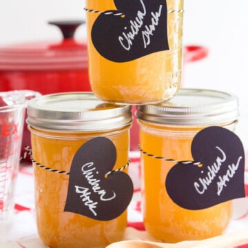 3 small Mason jars filled with chicken stock and black heart shaped labels.