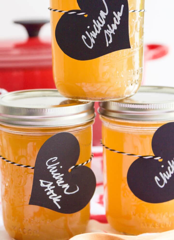 3 small Mason jars filled with chicken stock and black heart shaped labels.