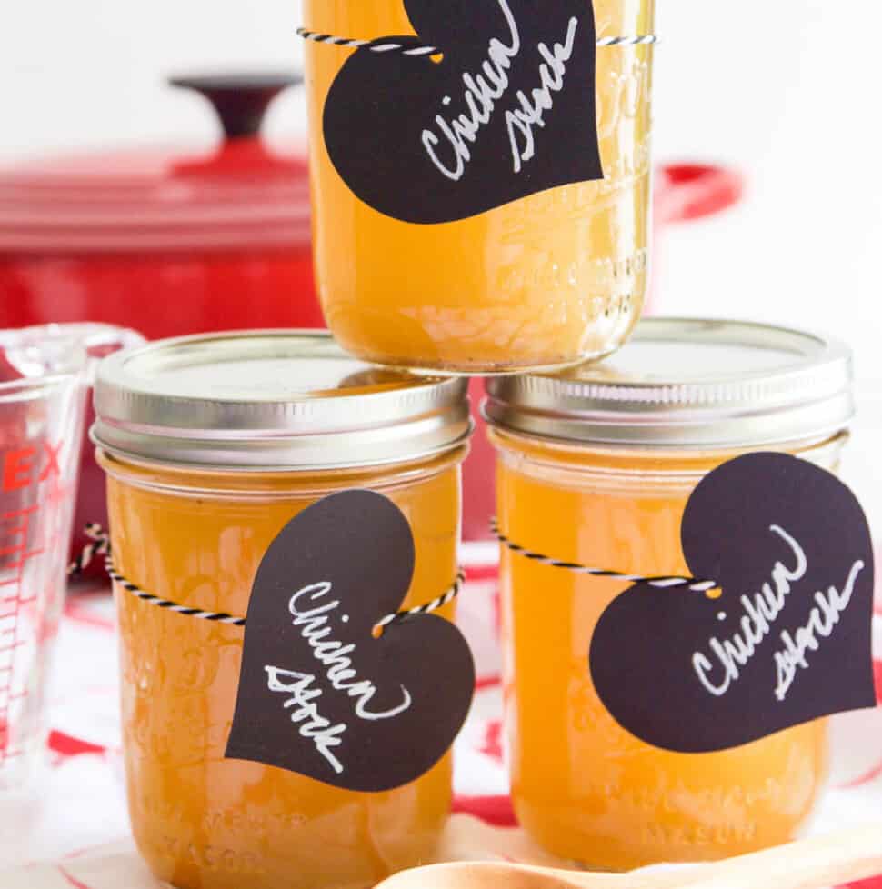 3 small Mason jars filled with chicken stock and black heart shaped labels.